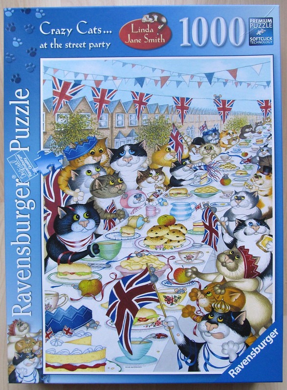 An illustration of many cats attending a festive outdoor street party with Union Jack flags and refreshments.