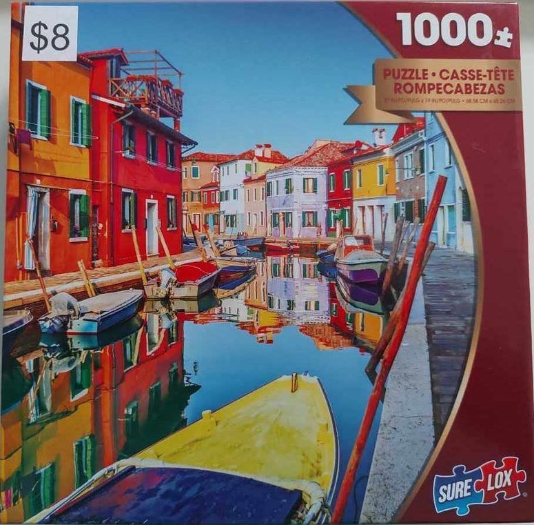 A vibrant canal scene in Burano, Italy, with colorful houses reflected in the water and small boats moored along the side.
