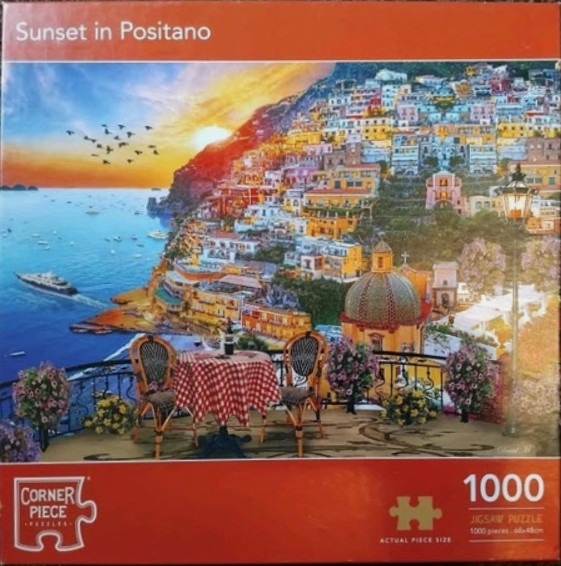 A balcony view of Positano, Italy at sunset with a table set for two overlooking the coastal cliffside houses.