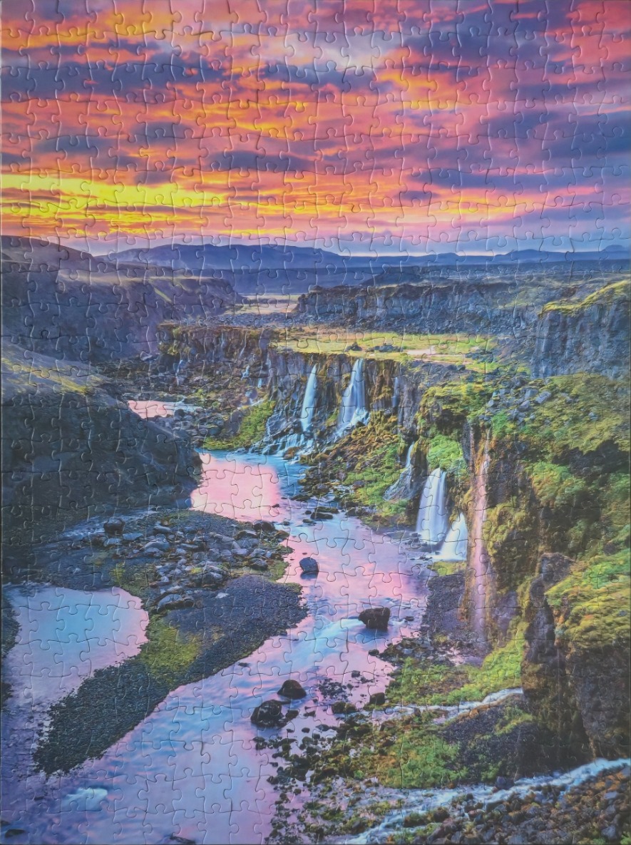 A scenic photograph of a river flowing past mossy cliffs at sunset with a vibrant pink and orange sky.