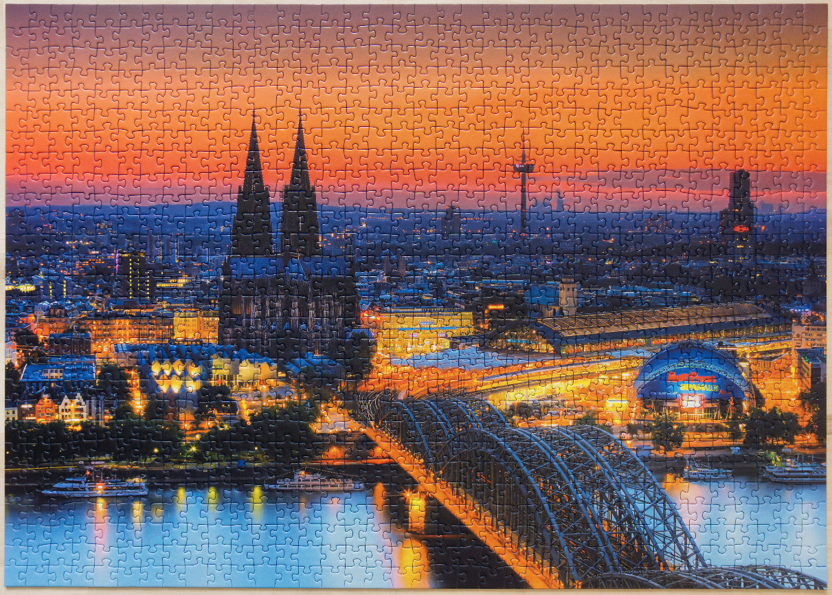 A twilight view of Cologne Cathedral and the Hohenzollern Bridge at sunset.