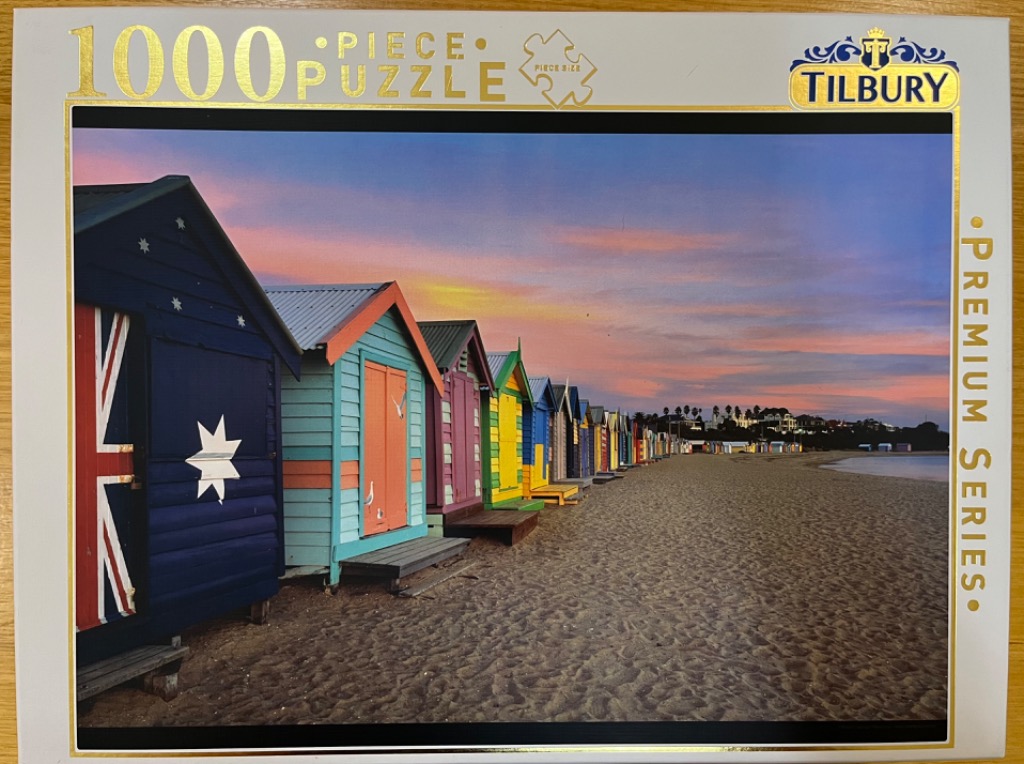 A row of colorful beach huts on a sandy beach at sunset, with the leftmost hut painted with an Australian flag.