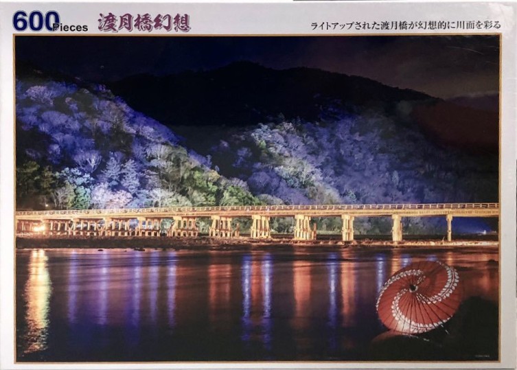 Night view of Togetsukyo Bridge in Kyoto with illuminated cherry blossom trees and a red parasol in the foreground.
