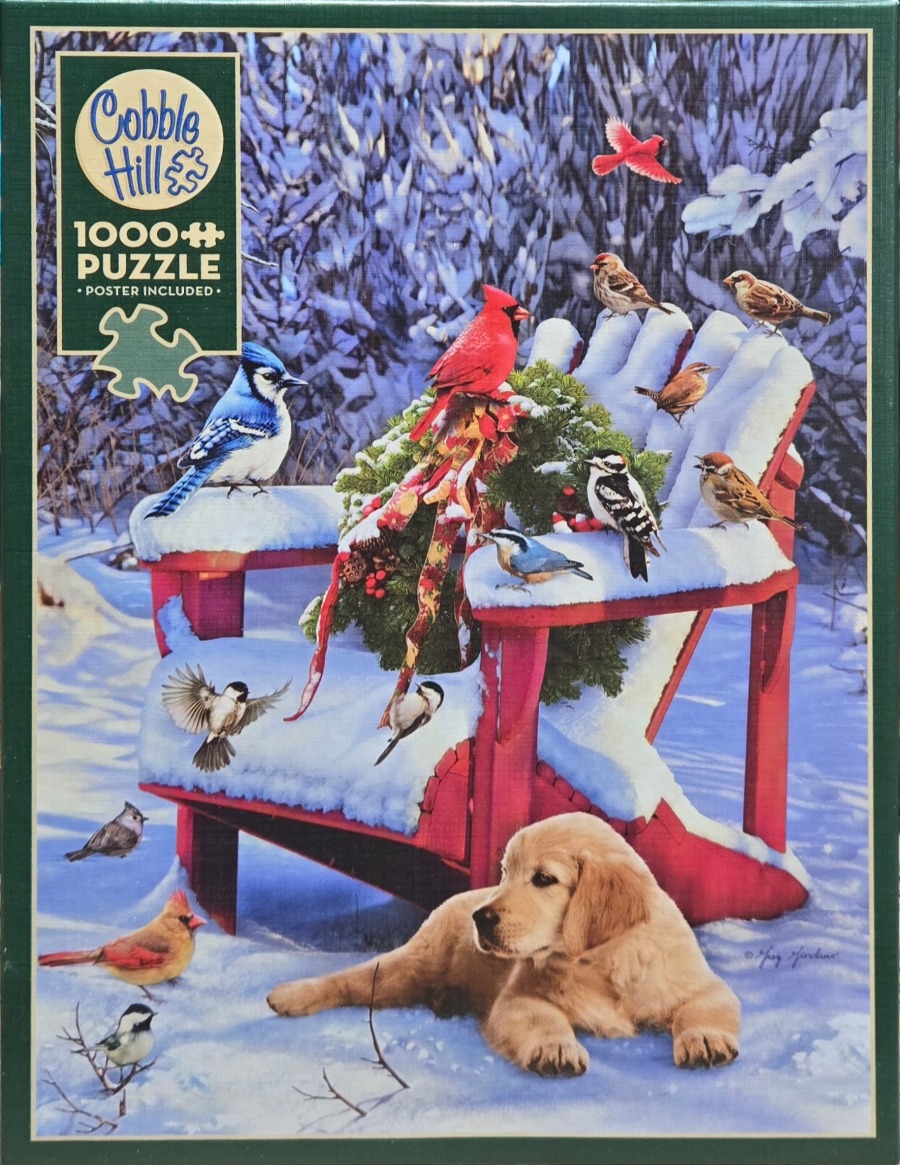 A golden retriever puppy lying in the snow in front of a red Adirondack chair filled with various winter birds.