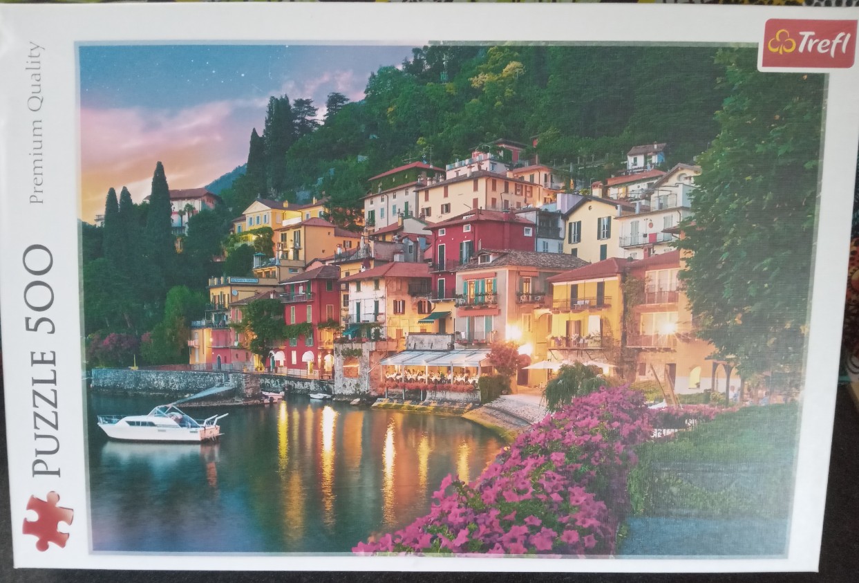 A colorful Italian village nestled on a hillside overlooking a calm lake at twilight.