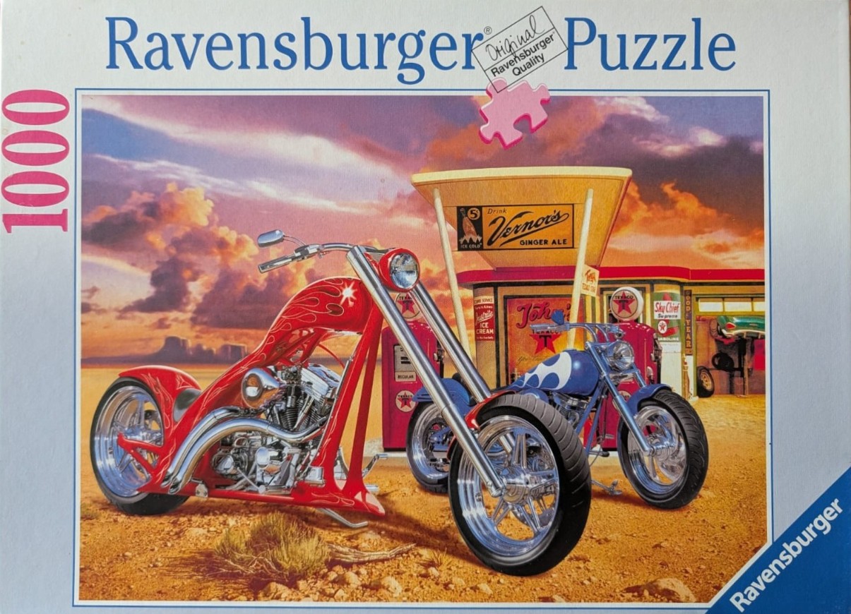 Two custom motorcycles parked at a vintage gas station during a desert sunset.