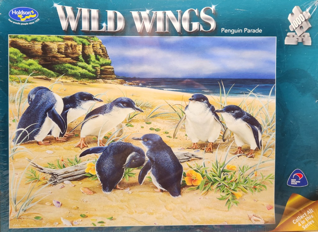 A group of little blue penguins on a sandy beach near a coastal cliff.