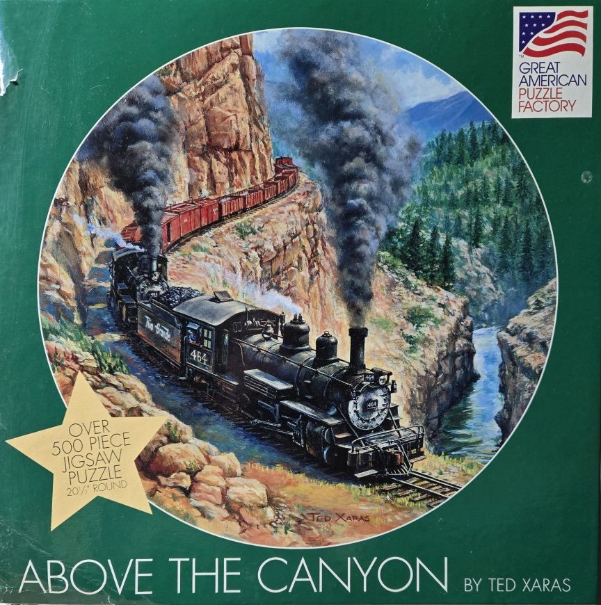 A steam train, Rio Grande #464, pulling red freight cars along a narrow rocky ledge above a canyon river.