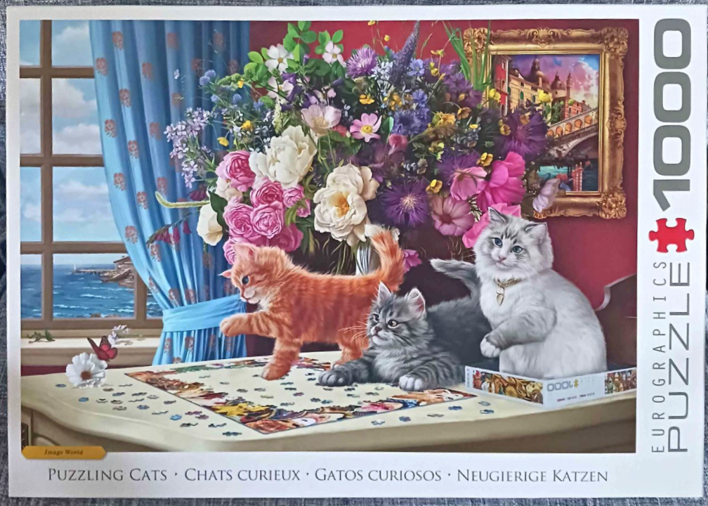 Three kittens playing on a table with a jigsaw puzzle, set against a background of flowers and a coastal window.