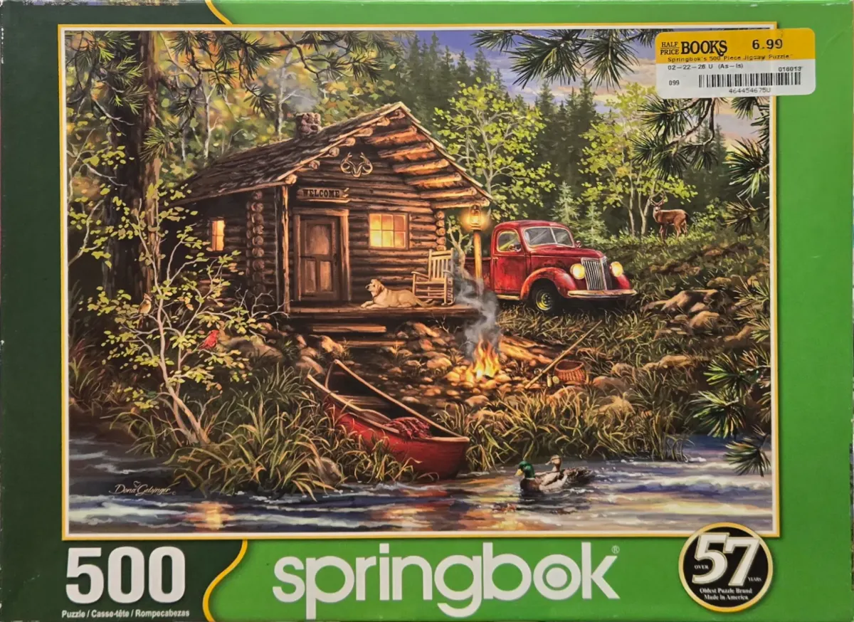 A cozy log cabin in the woods at twilight with a red pickup truck, a campfire, and a canoe by a stream.