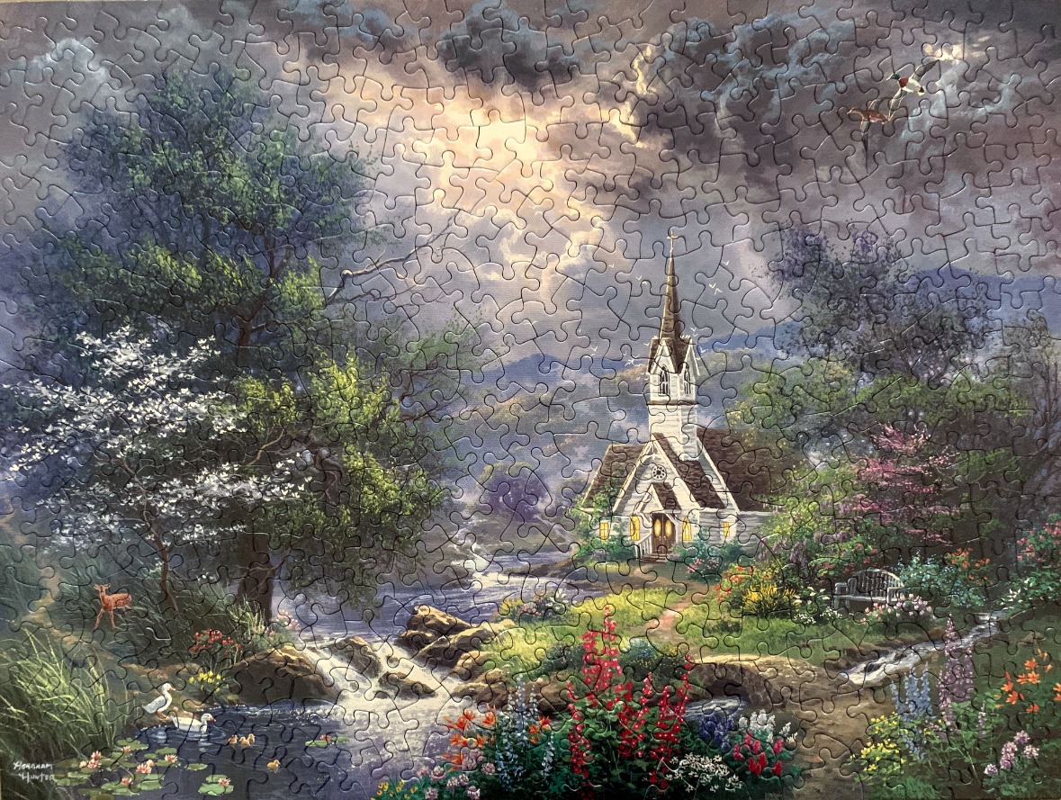 An idyllic church by a stream under a stormy sky with a sunlit break in the clouds.