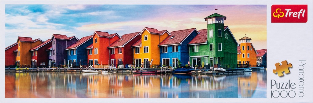 A panoramic view of a row of colourful, vibrant houses reflected in calm water at sunset.