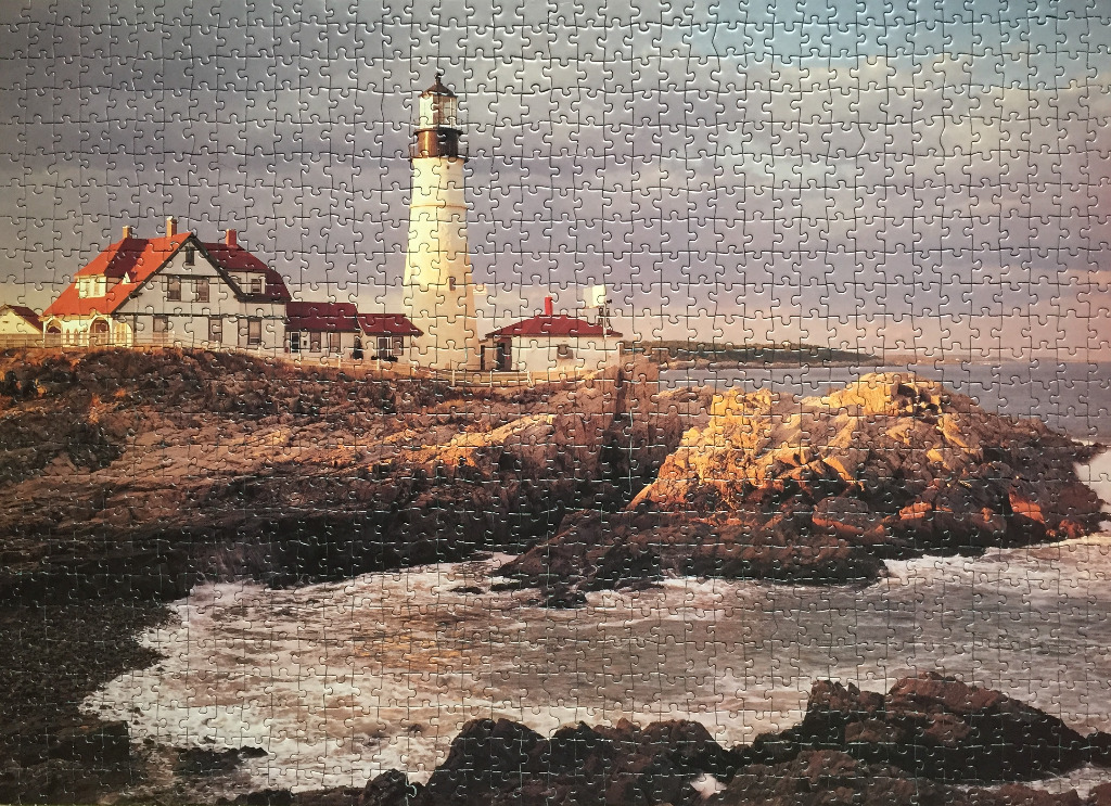 A scenic photograph of the Portland Head Light lighthouse and its keeper's house on a rocky coastline at sunset.
