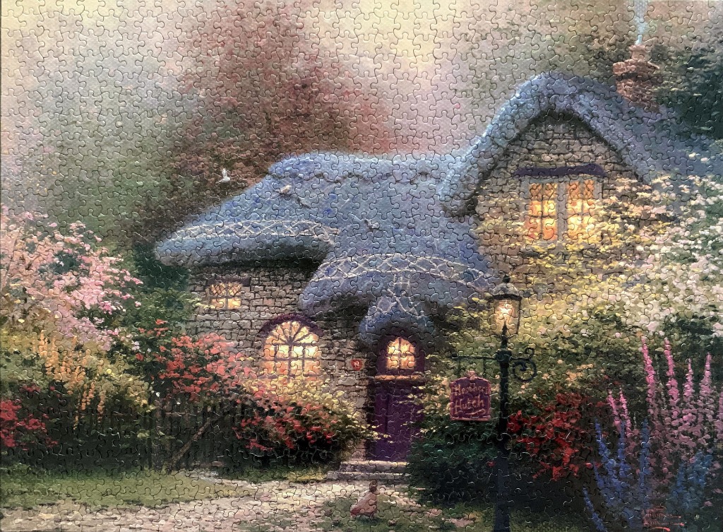 A cozy, stone cottage with a blue thatched roof nestled in a lush, blooming garden at twilight.