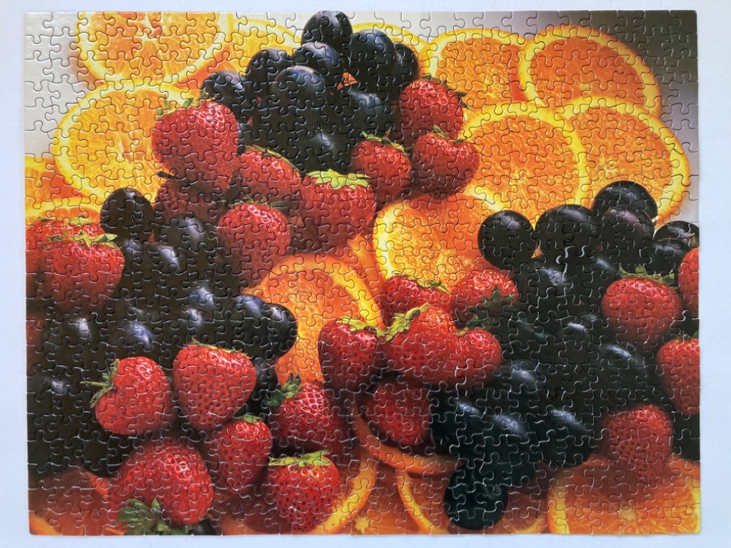 A close-up photograph of a vibrant fruit medley featuring oranges, strawberries, and dark grapes.