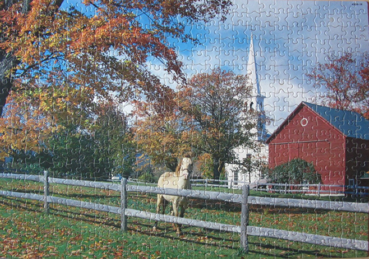 A horse stands in a fenced meadow with a red barn and a white church steeple in an autumn landscape.