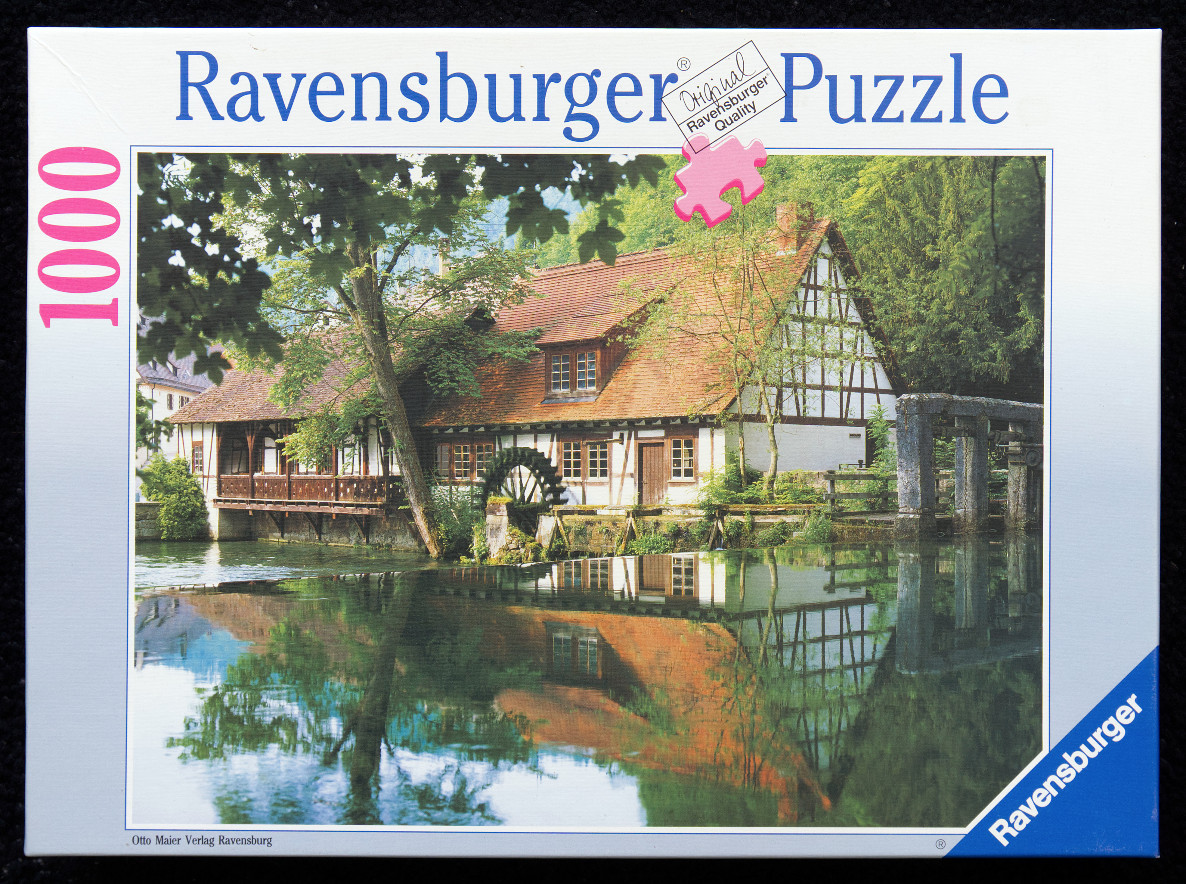 A scenic photograph of a half-timbered house with a waterwheel by a calm pond.