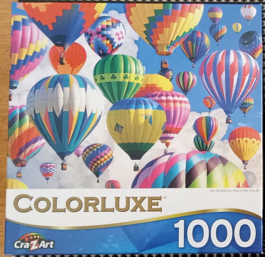 Many colorful hot air balloons floating in a bright blue sky with white clouds.