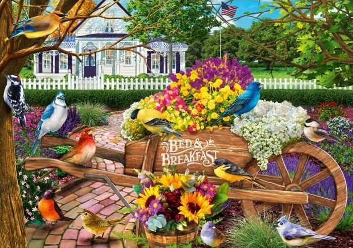 A wooden wheelbarrow overflowing with colorful flowers and surrounded by many different songbirds in a garden.