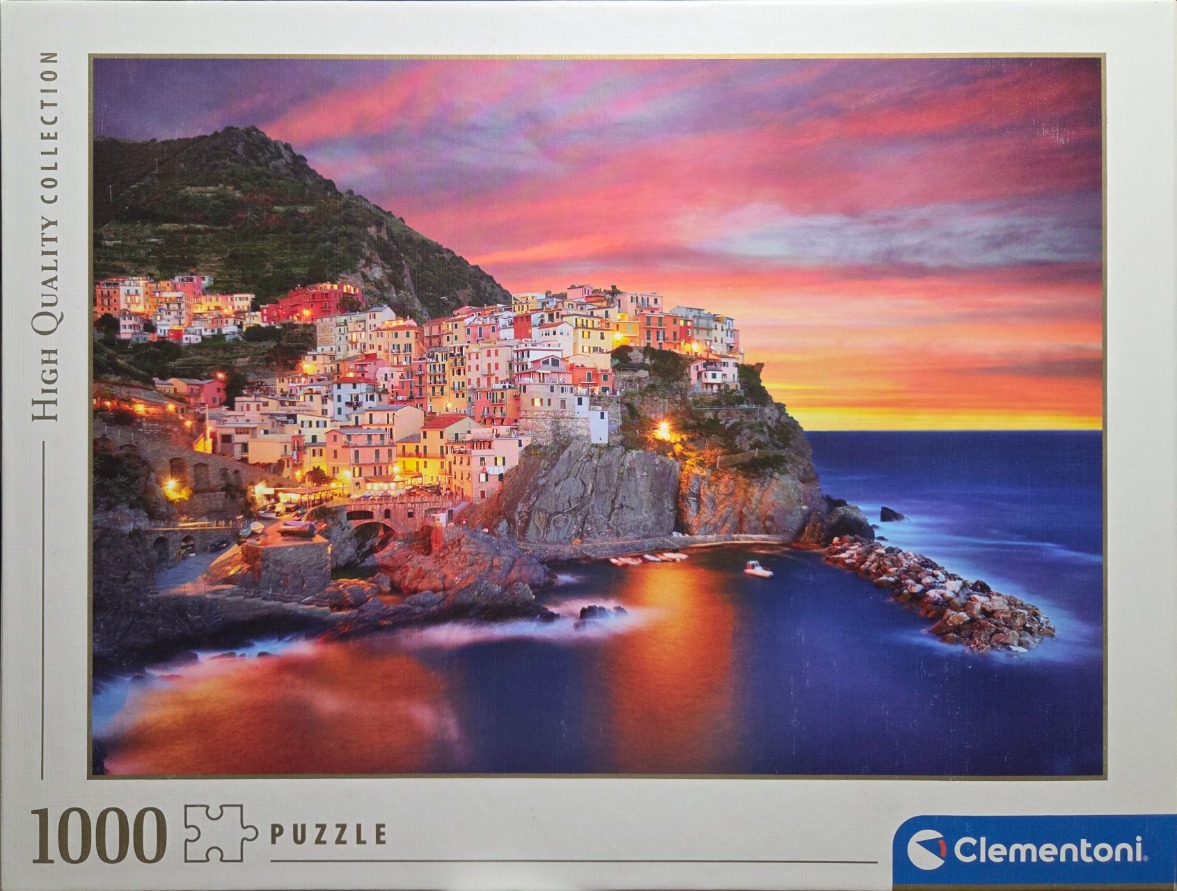 A photograph of the Italian village of Manarola at sunset, with colorful houses perched on a rocky cliff.