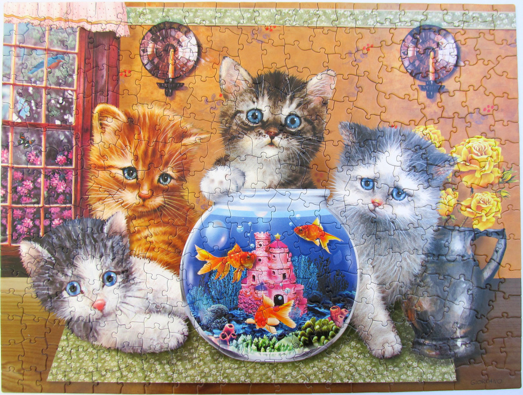 Four kittens gathered around a glass fishbowl containing goldfish and a pink castle.