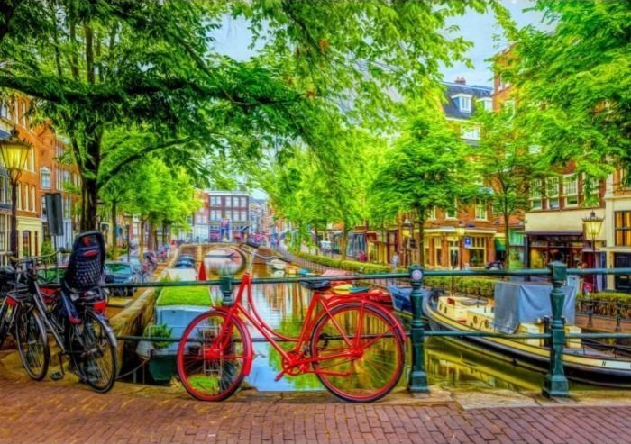 A bright red bicycle leans against a canal bridge railing in a lush, green Amsterdam cityscape.