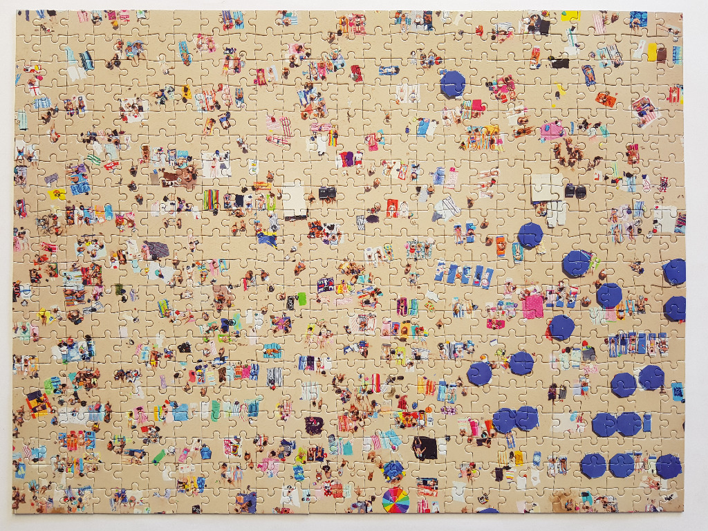 An aerial view illustration of a crowded sandy beach filled with small groups of people and colorful beach umbrellas.