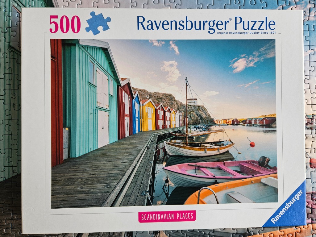 A row of colorful wooden boat houses lining a wooden pier with boats in the water at sunset.
