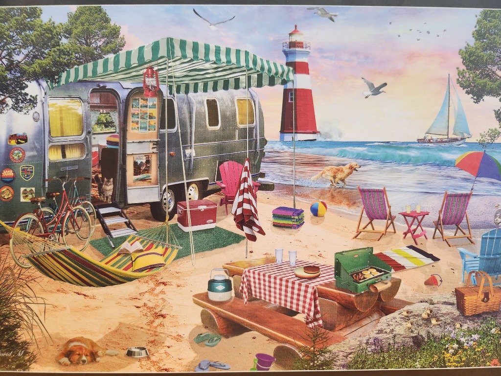 A vintage camper parked on a sunny beach next to a lighthouse, picnic table, and hammock.