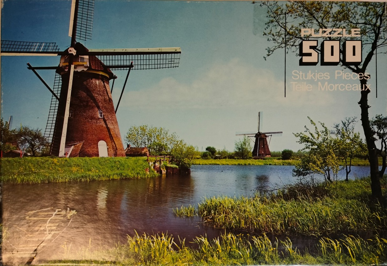Two rustic brick windmills situated along a reflective canal in a tranquil Dutch countryside landscape.