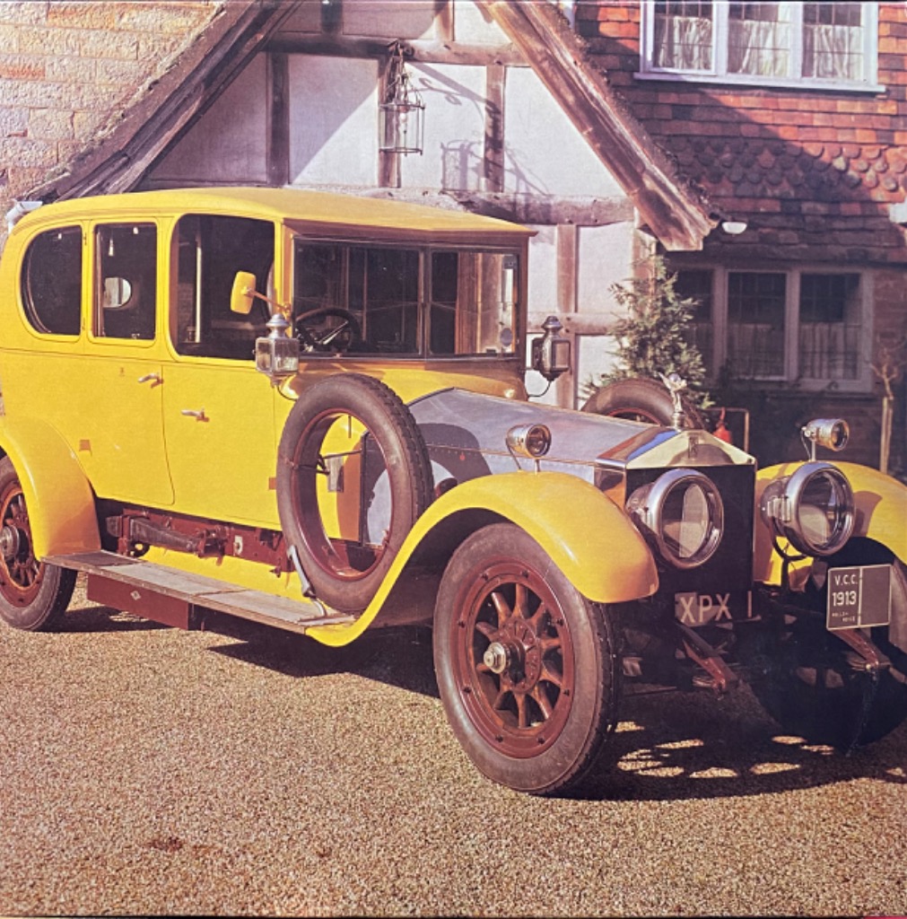 A vintage bright yellow 1913 automobile parked in front of a timber-framed house.