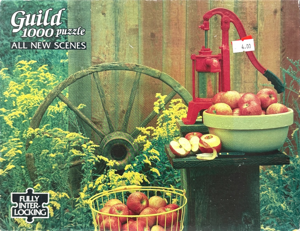 A vintage manual water pump and bowl of apples set against a wooden fence and wagon wheel in a rustic garden.