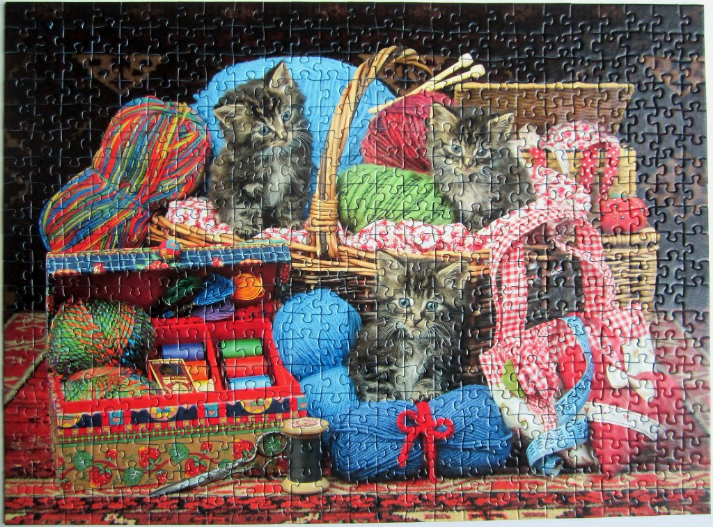 Three tabby kittens sitting among balls of colorful yarn, a sewing box, and knitting supplies.