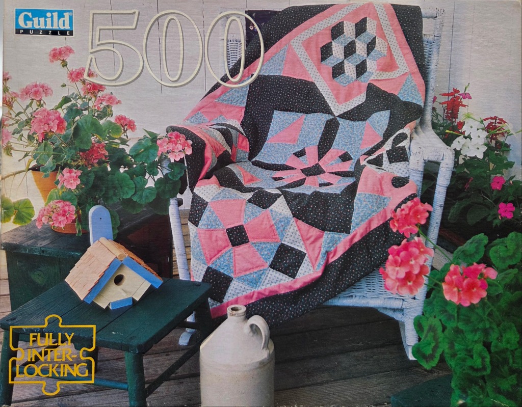 A handmade patchwork quilt draped over a white wicker chair, surrounded by potted flowers on a wooden deck.