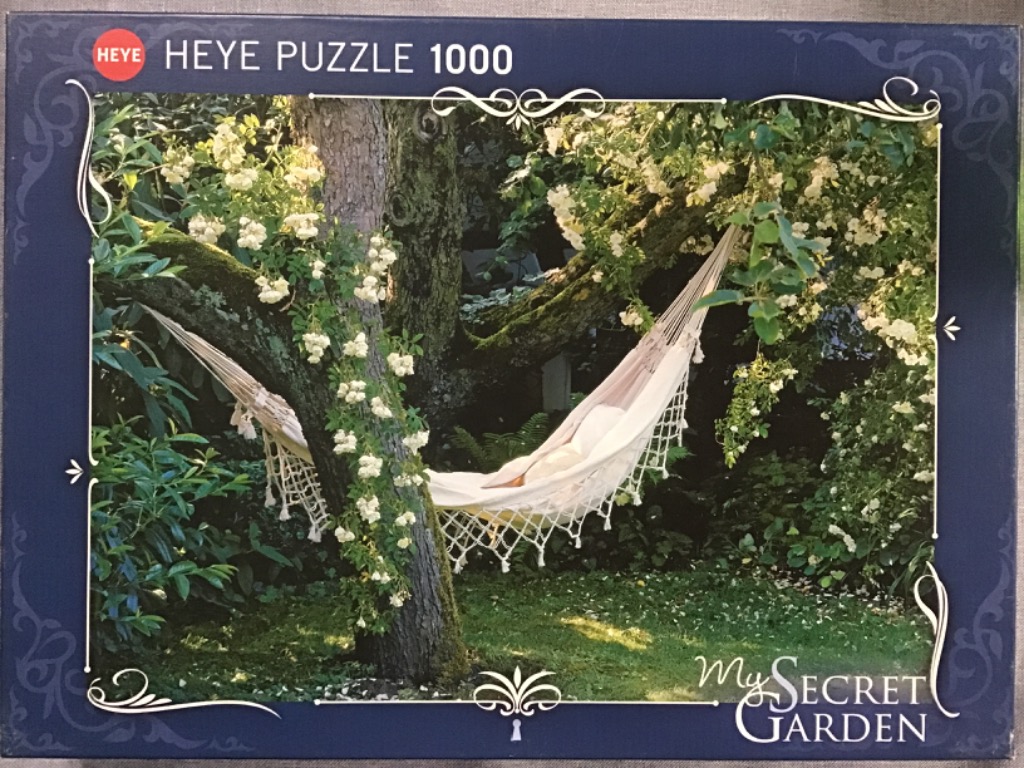 A cream-colored hammock hanging between two trees in a lush, blooming garden.