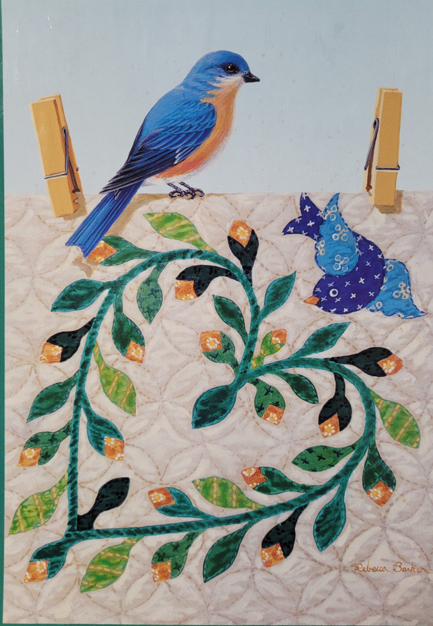 An illustration of a bluebird perched on a quilted fabric panel with a heart-shaped vine, secured by two clothespins.