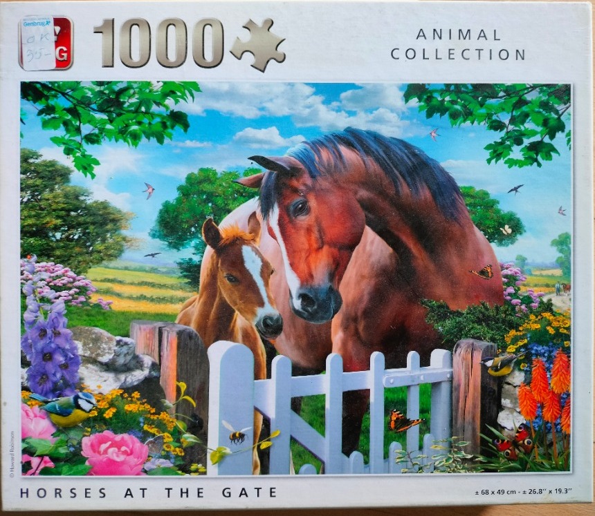 A bay mare and her foal standing behind a white wooden picket gate in a garden setting.