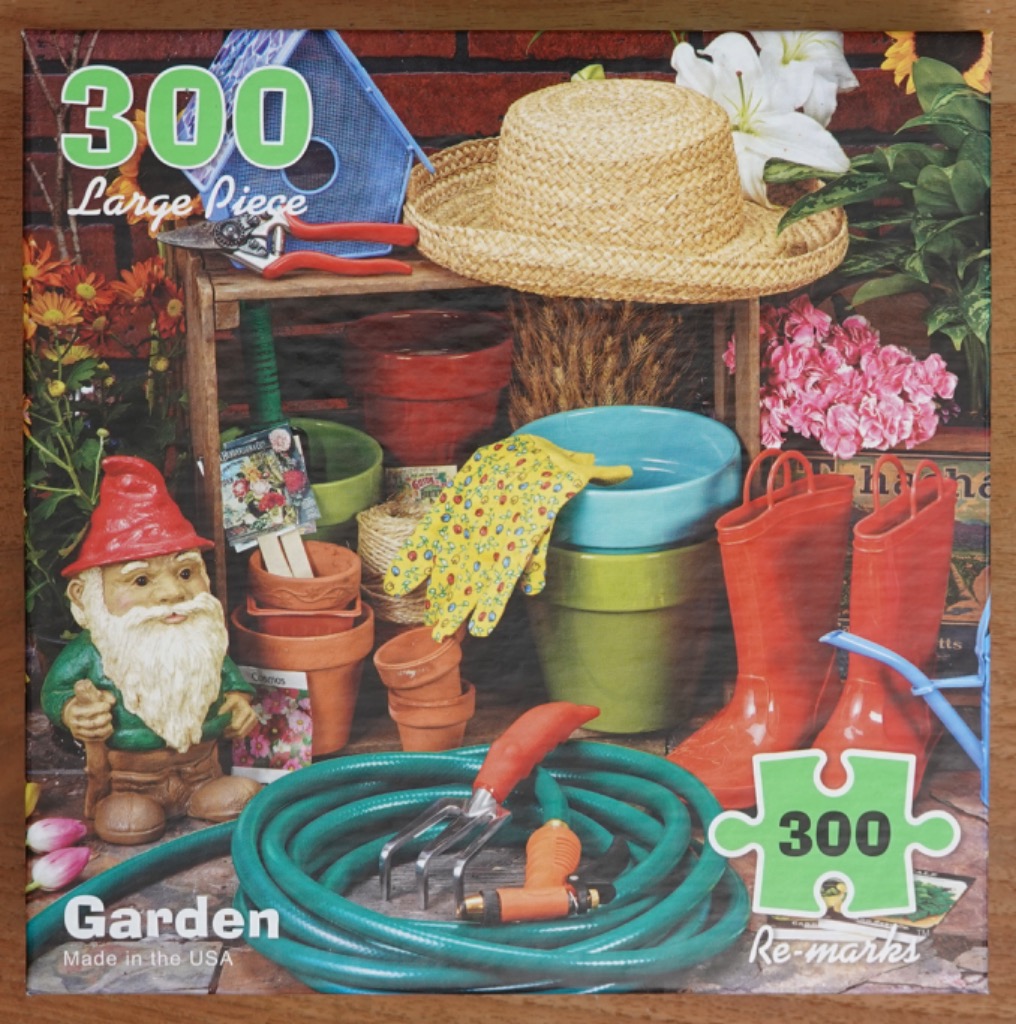 A still life arrangement of gardening tools, terracotta pots, a gnome, and bright red boots against a brick wall.