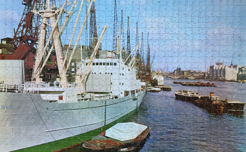 Cargo ship docked at a busy industrial river port with cranes under a blue sky