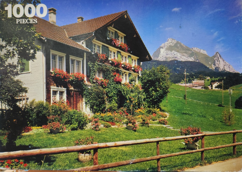 A traditional Swiss farmhouse adorned with flower boxes in front of a dramatic mountain landscape.