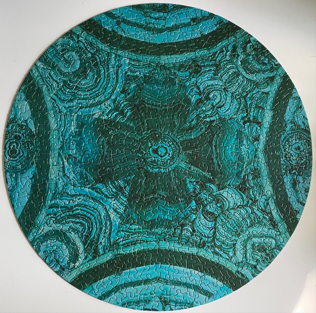 A circular pattern resembling malachite stone with concentric swirling rings in shades of teal, turquoise, and emerald.