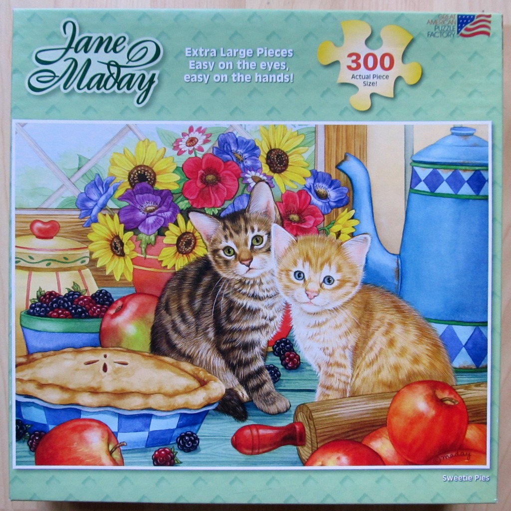An illustration of two small kittens sitting on a wooden table alongside a pie, fruit, and a blue teapot.