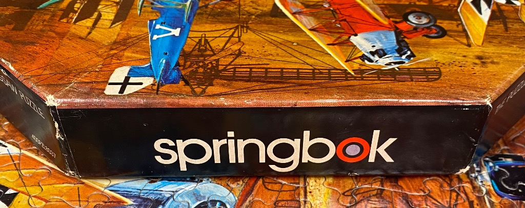Vintage biplane artwork on a puzzle box, featuring blue and red aircraft against a warm, sepia-toned background.