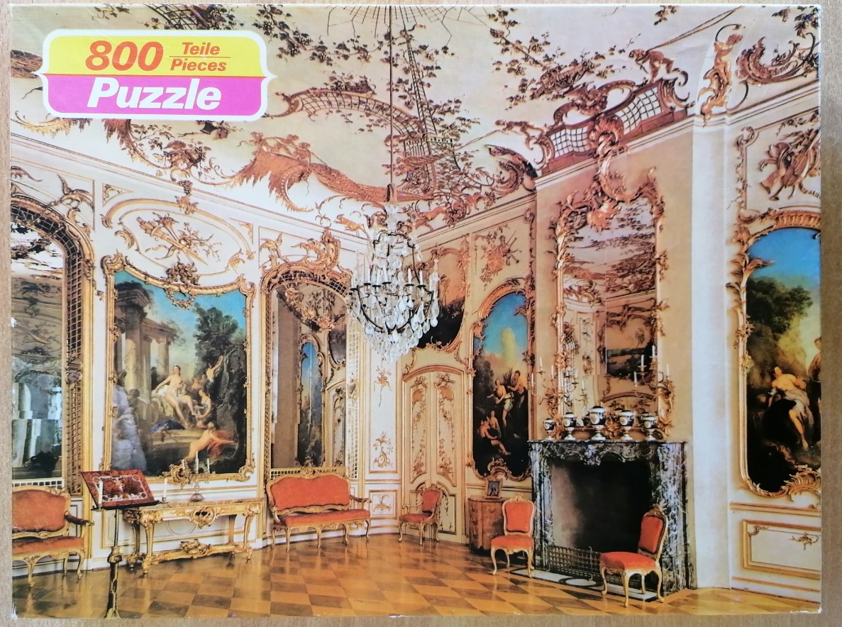Interior view of an ornate, Rococo-style palace room with gilded moldings, paintings, and a crystal chandelier.