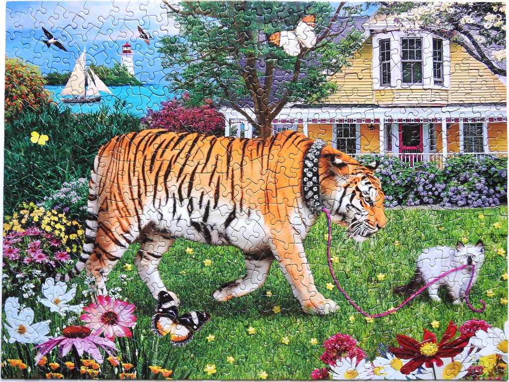 A tiger walking a small fluffy cat on a leash in a vibrant garden in front of a yellow house.