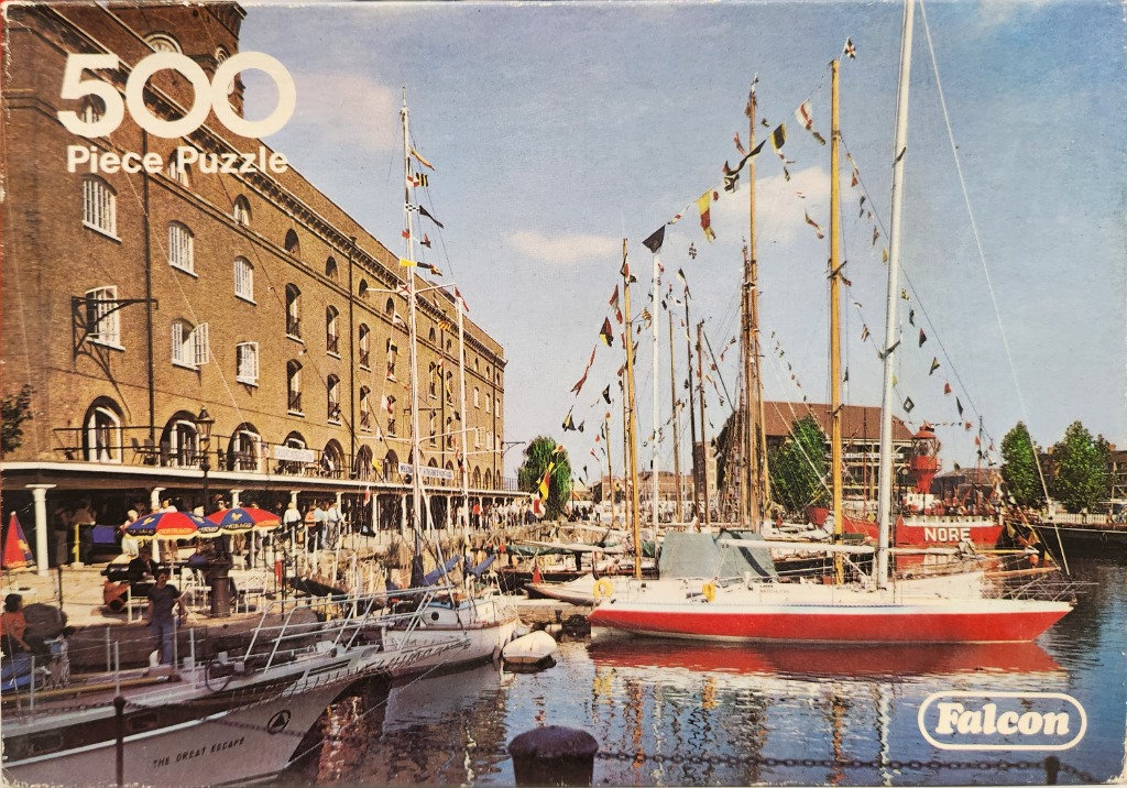 St Katharine Docks in London with historic brick warehouses and sailboats decorated with colorful signal flags.