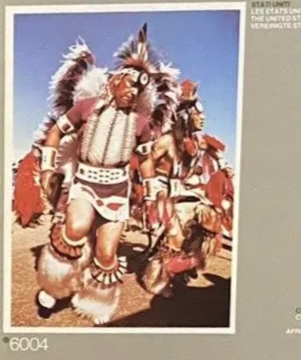 Two Native American men in traditional feathered regalia dancing outdoors.