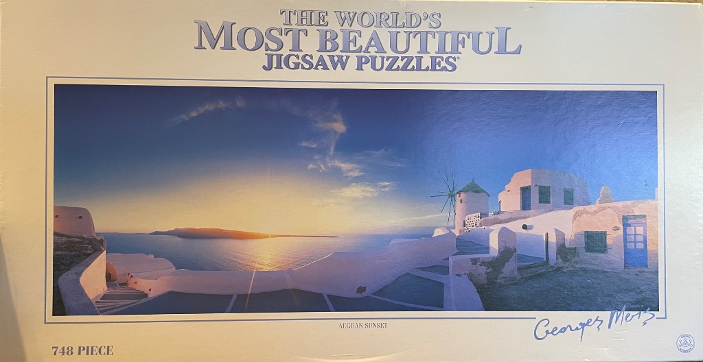 A panoramic photograph of a white stone village in Santorini overlooking the Aegean Sea at sunset.