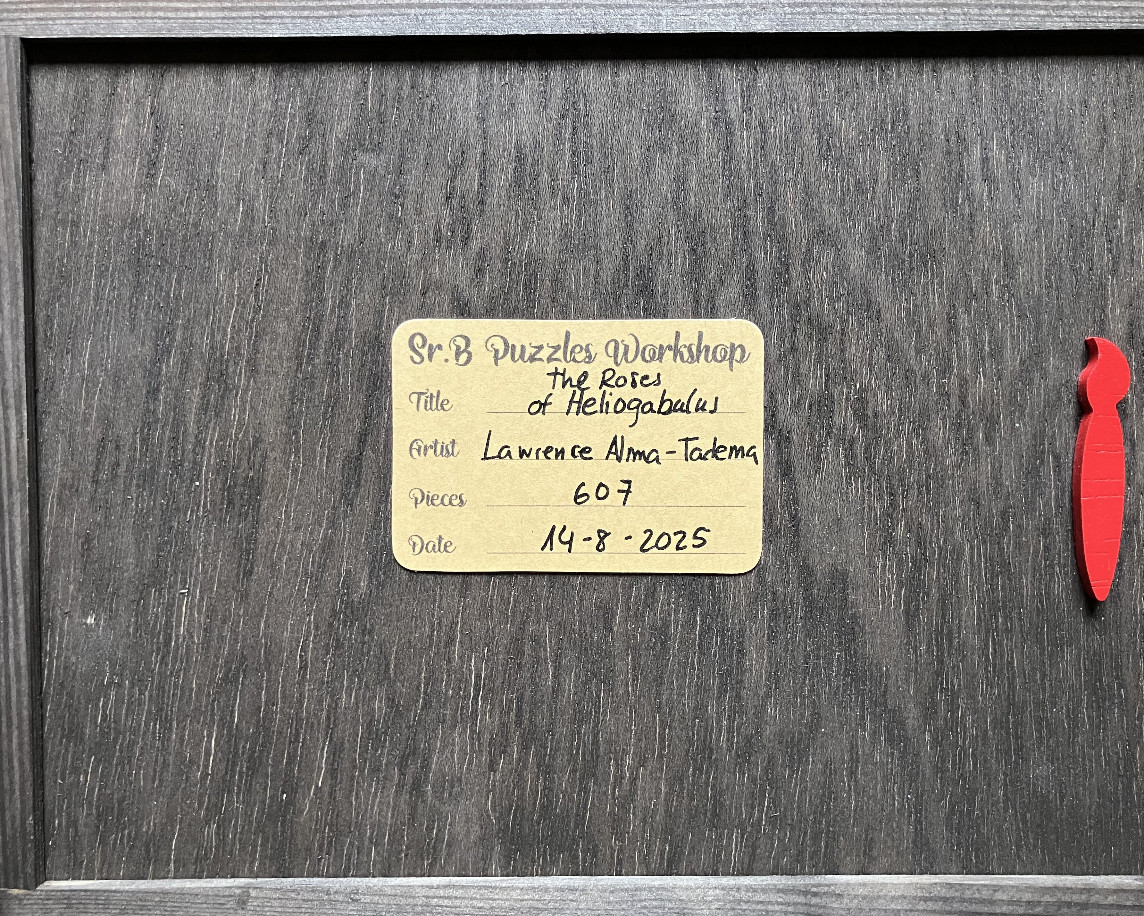 A rectangular tan label with handwritten text is centered on a grey wood-grain surface with a small red paintbrush icon.