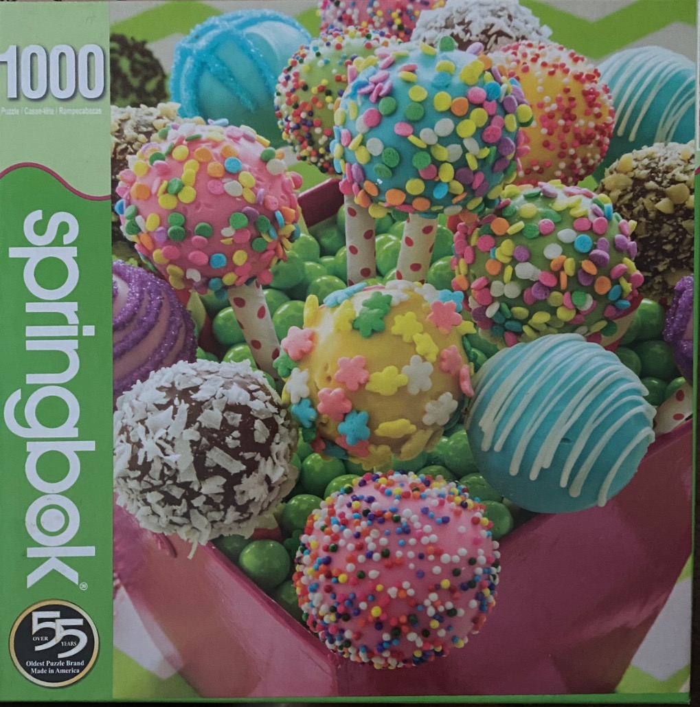 A close-up of a variety of colorful cake pops resting in a bed of green candy-coated chocolates.